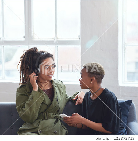 female friends using smartphone listening to music at home with woman wearing headphones female friends using smartphone listening to music at home with woman wearing headphones 122872715