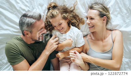Bed, love and family bonding, relax and having fun laughing and being playful in a bedroom together from above. Smile, play and happy child enjoy waking up in morning with playful, young parents 122872774