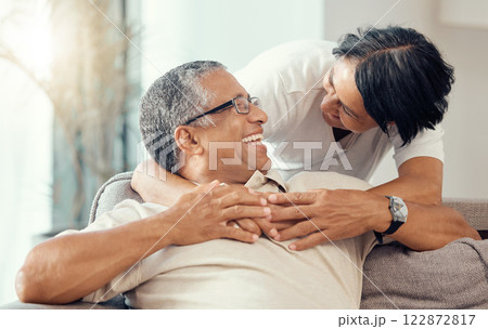 Love, senior couple and hug while laughing, bonding and sharing a romantic moment during retirement on the sofa at home. Joy, commitment and healthy relationship of an elderly man and woman together 122872817
