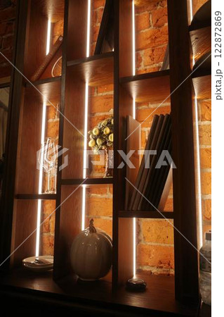 Loft-style shelving, with a red brick wall and lighting. Glasses, books and flowers 122872869