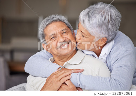 Happy Mexico senior couple kiss on living room sofa for love, care and trust in romantic relationship at house or home. Elderly people or retirement man and woman smile, hug and kissing face cheek 122873061