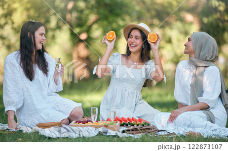 Diversity, Islamic and friends on a fruit picnic on grass in nature enjoying orange, watermelon and fun jokes. Muslim, smile and happy women laughing and smiling together at a natural park for lunch 122873107