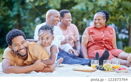 Portrait of a black father and child at a picnic with family in an outdoor green garden during spring. Smile, happy and african people eating healthy fruit at a outside celebration in a park. 122873764