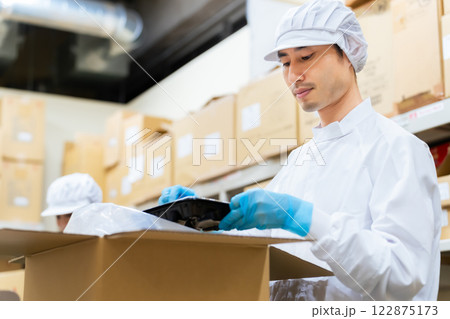 バックヤードで食品を箱詰めする白衣の男性　給食センター　宅配食　包装工場 122875173