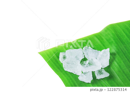 Pieces of alum stone on green banana leaf against white background. Concept of the connection between natural minerals and plant based ingredients in traditional practices and holistic wellness. 122875314