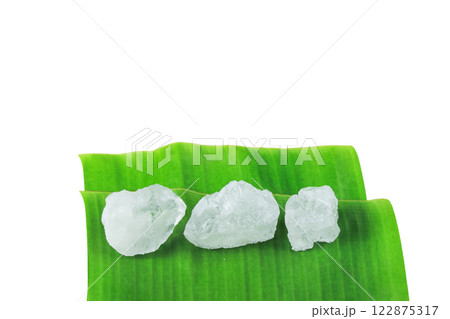Pieces of alum stone on green banana leaf against white background. Concept of the connection between natural minerals and plant based ingredients in traditional practices and holistic wellness. 122875317