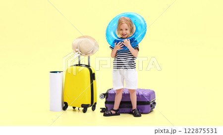 Smiling girl playfully wearing inflatable swim ring around head, smiling, standing next to suitcase, ready for beach trip Smiling girl playfully wearing inflatable swim ring around head, smiling, standing next to suitcase, ready for beach trip 122875531