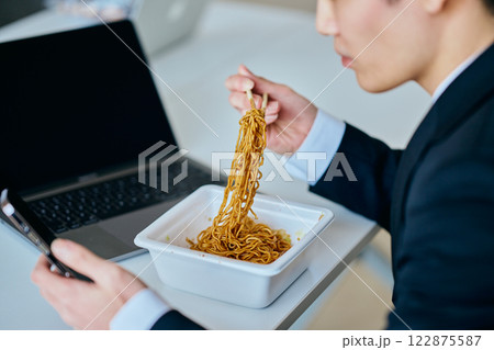カップ焼きそばを食べながらスマホを操作する20代の若い男性 122875587