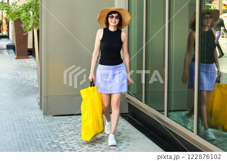 A woman with a bag of new purchases walks along the modern city streets smiling happily with joy 122876102