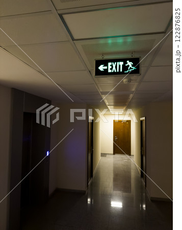 Corridor with illuminated green sign helping to find emergency exit 122876825
