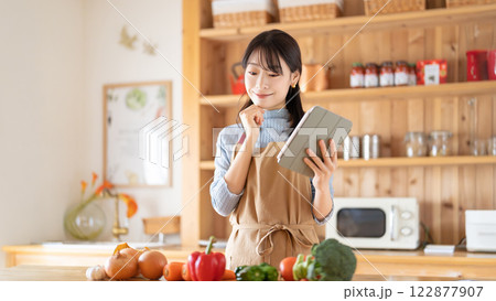 タブレットを見ながら料理をする笑顔の女性 122877907