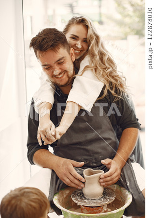 Mutual creative work. Young beautiful couple in casual clothes and aprons. People creating a bowl on a pottery wheel in a clay studio. Mutual creative work. Young beautiful couple in casual clothes and aprons. People creating a bowl on a pottery wheel in a clay studio. 122878010