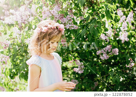young girl with curly blonde hair standing among blooming lilac bushes in sunlit garden. soft lighting and natural setting create dreamy atmosphere, evoking themes of innocence, childhood, young girl with curly blonde hair standing among blooming lilac bushes in sunlit garden. soft lighting and natural setting create dreamy atmosphere, evoking themes of innocence, childhood, 122878052