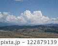 Panoramic photo of white air clouds floating low over a mountain range in sunny weather. 122879139