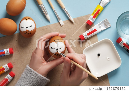 Drawing a sleeping owl on an eggshell. Step 2: Draw the beak. Preparation for Easter celebration. Acrylic paints in tubes, water, brushes. 122879182