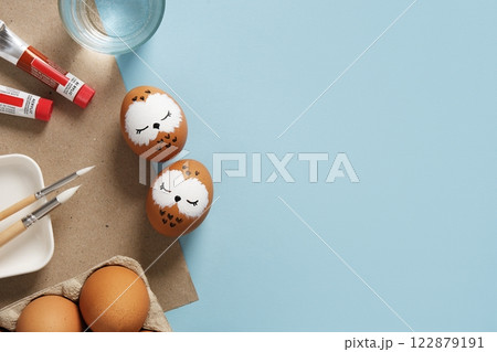 Easter eggs with sleeping owls, hand-painted with acrylics, on a background of paints, brushes and palettes. Copyspace 122879191