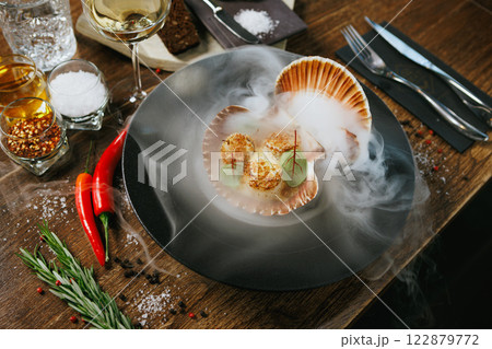 Seared scallops with avocado puree and microgreens in a shell. Presented with dramatic dry ice smoke. Exquisite seafood dish in a high-end dining setting 122879772