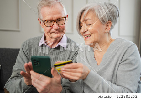 Senior couple man woman shopping online with smartphone paying with credit card. Old people buying on Internet enter credit card details at home indoors. Online shopping delivery service ecommerce 122881252
