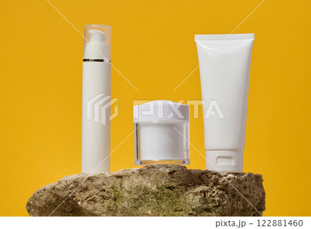 White plastic jars, tube stand on a stone on a yellow background. Container for cosmetics, cream White plastic jars, tube stand on a stone on a yellow background. Container for cosmetics, cream 122881460