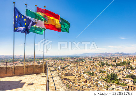 Granada town in Spain from the Alhambra complex. Panoramic city view with flags waving under a clear blue sky. A picturesque scene of urban landscape and national symbols. Granada town in Spain from the Alhambra complex. Panoramic city view with flags waving under a clear blue sky. A picturesque scene of urban landscape and national symbols. 122881768