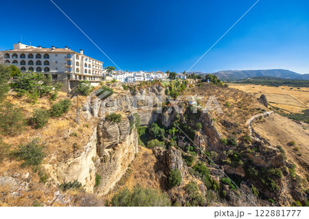 Ronda town in Spain. White village perched on dramatic cliffs, overlooking a vast, dry landscape under a clear blue sky. 122881777