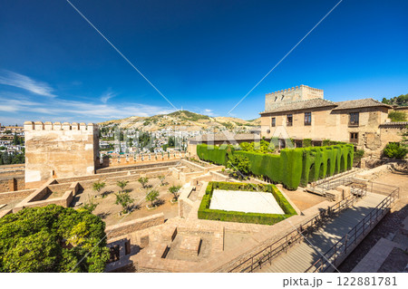 The Mexuar, part of the Alhambra complex, Granada, Andalusia, Spain. Ancient palace gardens with manicured hedges and a stone tower under a clear blue sky. 122881781
