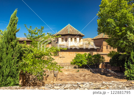 Alhambra complex in Granada town, Andalusia, Spain. Remains of the Rawda mausoleum. Ancient architecture nestled amongst lush greenery under a vibrant blue sky. A peaceful courtyard scene. Alhambra complex in Granada town, Andalusia, Spain. Remains of the Rawda mausoleum. Ancient architecture nestled amongst lush greenery under a vibrant blue sky. A peaceful courtyard scene. 122881795
