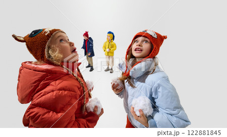 Kids, dressed warm winter jackets and knitted hats, holding snowballs, looking excited and playful, preparing for winter game against white background. Kids, dressed warm winter jackets and knitted hats, holding snowballs, looking excited and playful, preparing for winter game against white background. 122881845