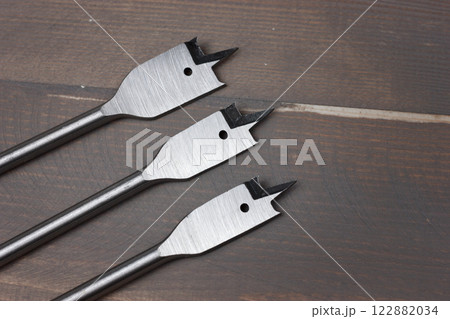 Three spade drill bits on a wooden surface. 122882034