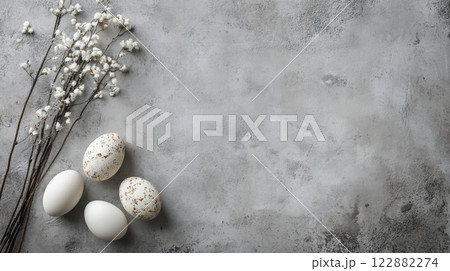 Easter white and speckled eggs alongside delicate dried flowers on a textured grey concrete background 122882274