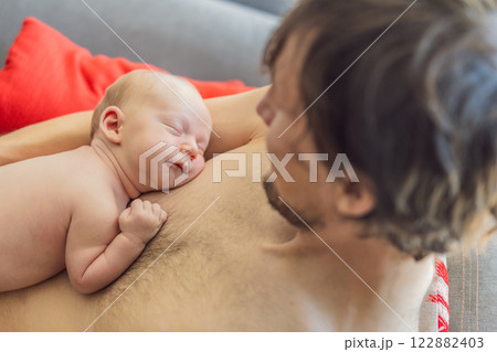 A newborn baby rests peacefully on the father's chest, feeling the warmth and heartbeat of his parent. A tender moment of bonding, love, and security, symbolizing the deep connection between father 122882403