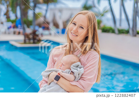 A mother holds her baby near a tropical pool, surrounded by lush greenery. This heartwarming moment captures family bonding, maternal love, and the serene beauty of a tropical getaway, perfect for 122882407
