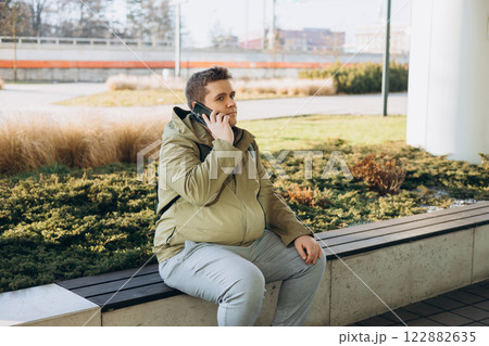Business phone conversation. Happy blonde 30s man talking on smartphone on the city street. Communication and gadgets, connection concept. Man holding on cell smartphone while relaxing outdoors 122882635