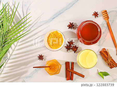 Golden turmeric latte with ginger, cinnamon, anise and honey spices on a sunny table. Weight loss and alternative medicine concept, immunity booster during pandemic, Indian cuisine advertisement 122883739