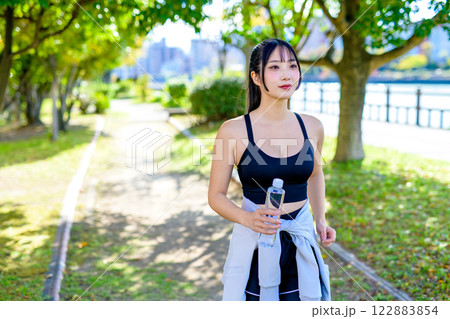 木漏れ日の道を歩きながら水分補給するかっこいい女性　ダイエット　エクササイズ　運動　 122883854