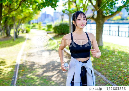 木漏れ日の道を歩きながら水分補給するかっこいい女性　ダイエット　エクササイズ　運動　 122883858