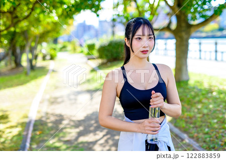 木漏れ日の道を歩きながら水分補給するかっこいい女性　ダイエット　エクササイズ　運動　 122883859