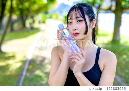 木漏れ日の道を歩きながら水分補給するかっこいい女性　ダイエット　エクササイズ　運動　 122883936