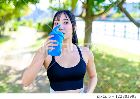 木漏れ日の道を歩きながら水分補給するかっこいい女性　プロテイン　エクササイズ　運動　 122883995