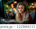 A young woman engages intensely with her gaming setup, wearing a headset and eyeglasses, in a lively esports arena filled with colorful lights, immersed in the competitive atmosphere. 122884215