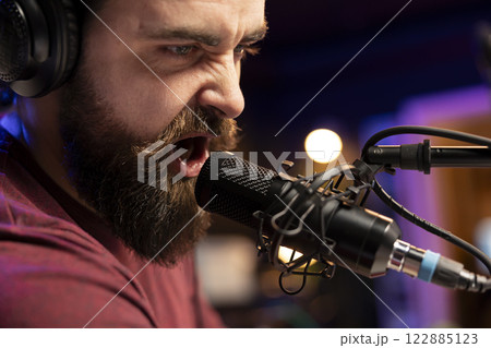 Skilled music producer recording his lyrics on microphone to create tracks with mixing and mastering gear. Young professional artist composing soundtracks on stereo equipment. Skilled music producer recording his lyrics on microphone to create tracks with mixing and mastering gear. Young professional artist composing soundtracks on stereo equipment. 122885123