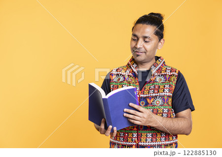 Indian man reading book, having fun and enjoying characters and plot, isolated over studio background. Relaxed person browsing novel, enjoying leisure time, appreciating literature 122885130
