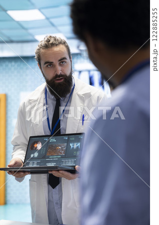 Neurology specialist examines magnetic resonance imaging brain scan with his team in a meeting, looking at tomography for accurate neuroscience diagnosis. Diverse team of neurologist doctors. 122885255