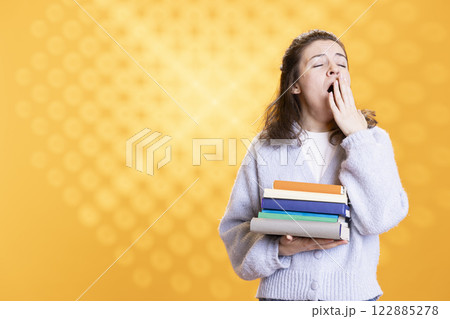 Tired woman yawning while holding books conveying boredom of reading concept, studio background. Exhausted person with novels in arms showing dissatisfaction for tedious literature 122885278