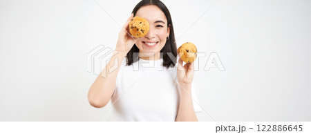 Close up portrait of smiling korean woman, shows tasty cupcakes, eating cake and looking happy, pastry and bakery concept 122886645