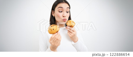 Close up portrait of asian girl eats cupcakes with happy face, isolated on white background Close up portrait of asian girl eats cupcakes with happy face, isolated on white background 122886654
