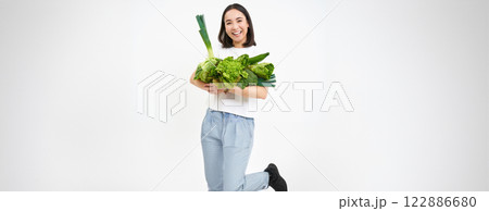 Image of smiling asian woman, vegetarian with lots of green vegetables, eating oranic food, isolated on white background 122886680