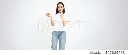 Portrait of asian girl with pensive face, holds cupcake with thinking face, isolated on white background Portrait of asian girl with pensive face, holds cupcake with thinking face, isolated on white background 122886688
