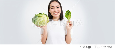 Close up portrait of asian woman, biting lettuce, eating green cabbage and smiling, white background Close up portrait of asian woman, biting lettuce, eating green cabbage and smiling, white background 122886768