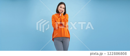 Beauty and wellbeing. Young brunette woman laughing and smiling, touching her natural healthy face, standing over blue studio background 122886808